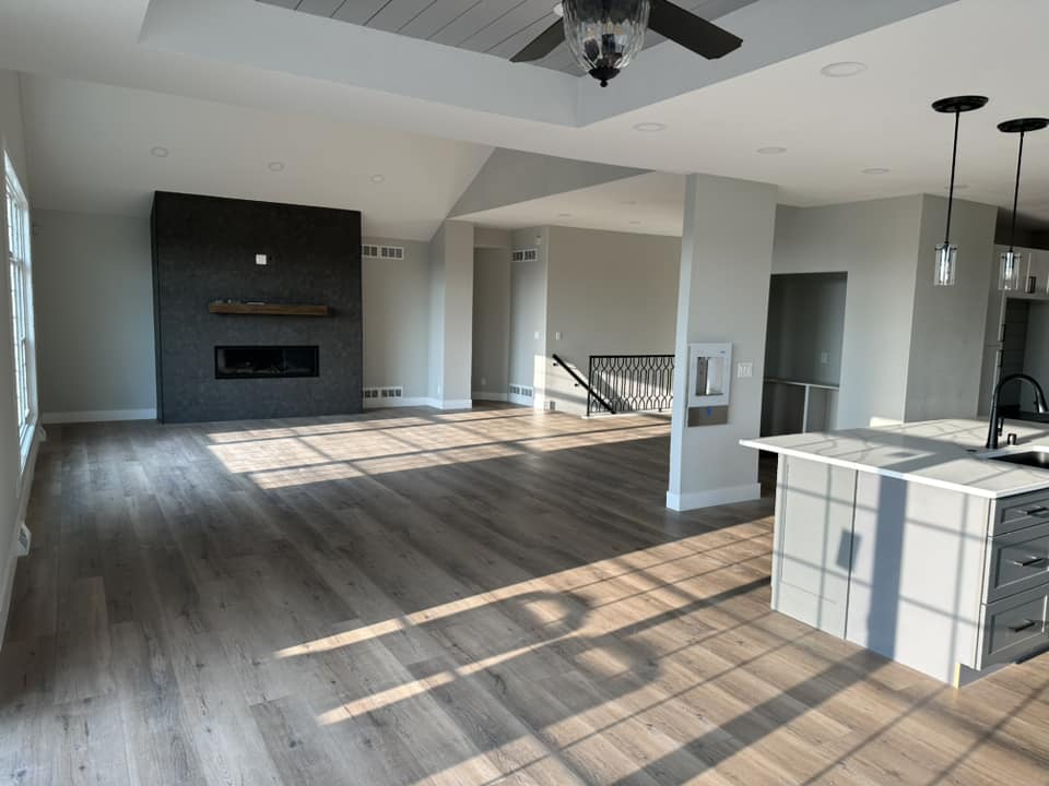 Finished open-plan living area with dark tile fireplace wall, hardwood floors, wrought-iron stair railing, and shiplap tray ceiling